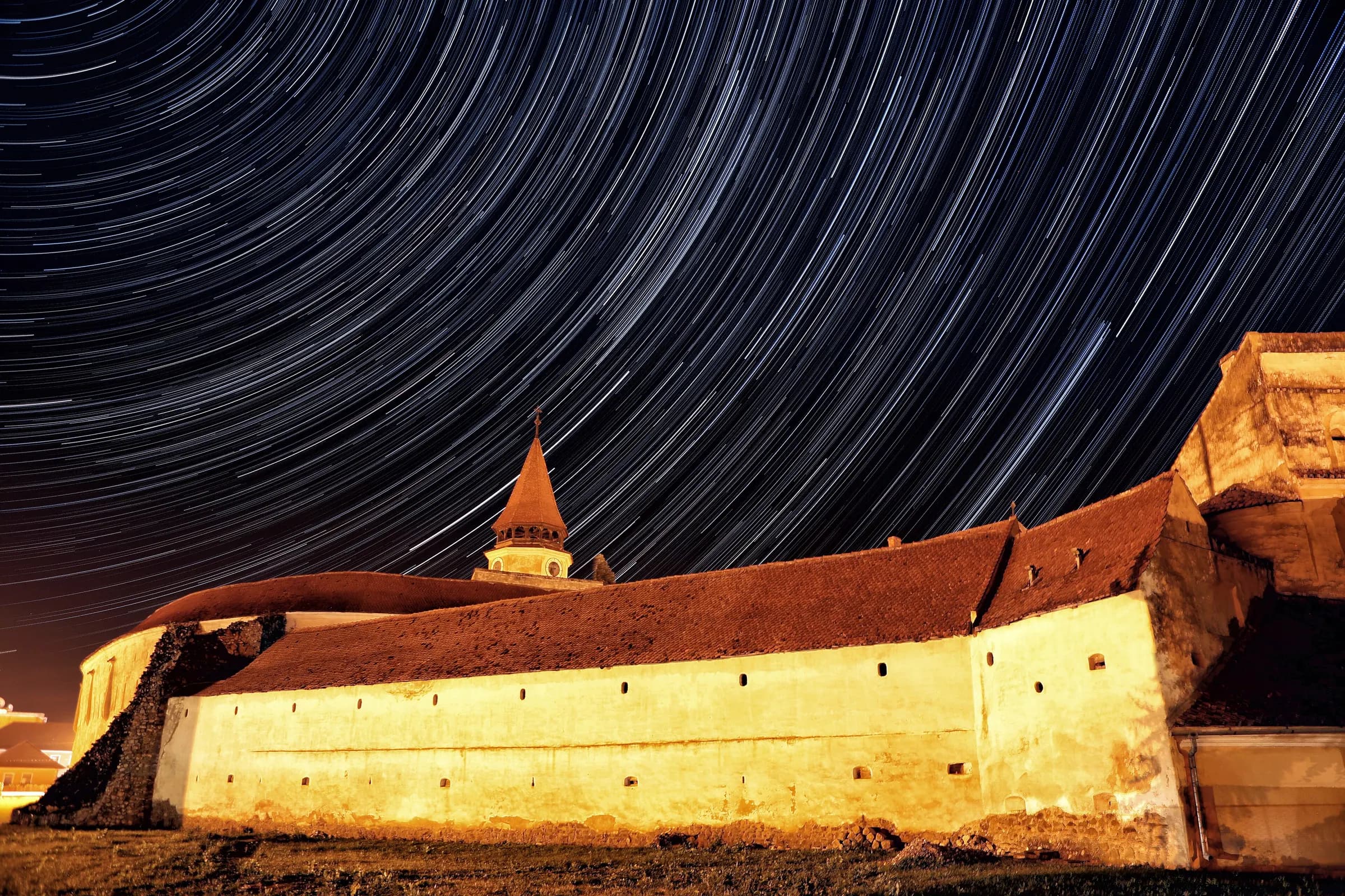 Star trails over the lit walls of the Prejmer fortified church at night