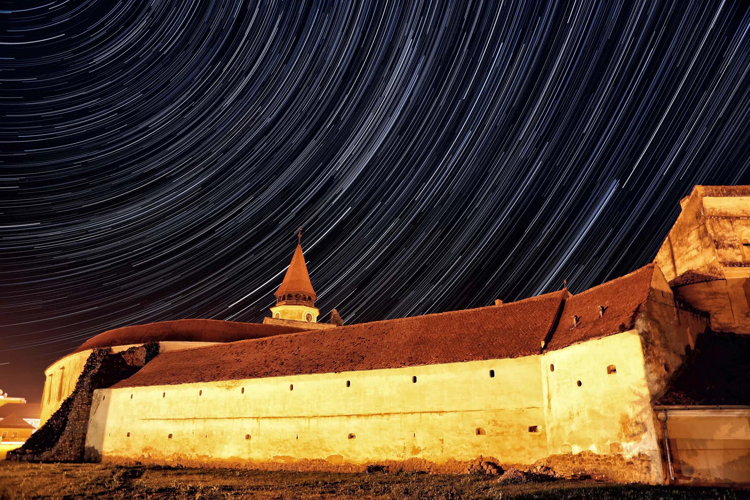 Star trails over the lit walls of the Prejmer fortified church at night